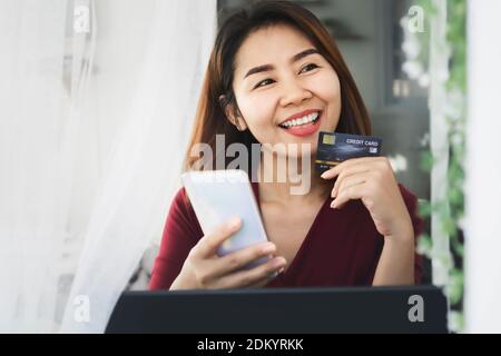 smile Asian girl happy shopping online from home hand holding credit card and smart phone Stock Photo