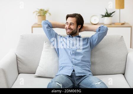 Relaxed Guy Sitting Holding Hands Behind Head On Sofa Indoor Stock Photo