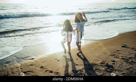 The picture shows a back view of two unrecognizable little girls holding hands in front of the sea on a sunny afternoon. Concept of friendship Stock Photo