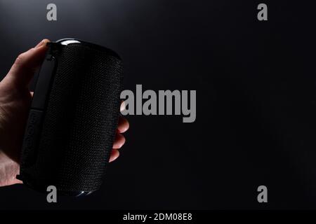 Black wireless portable speaker in hand, on black background with copyspace.