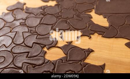 Rolled raw cocoa dough with cut out decorative shapes for Christmas gingerbread cookies. Close-up of various sweets for baking of yummy pastry on wood. Stock Photo