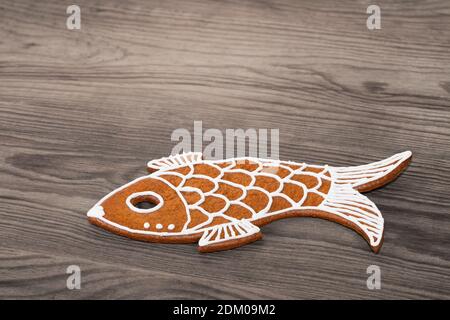 Sweet fish baked from Christmas gingerbread cookie on a wood background. Close-up of yummy biscuit decorated with white icing. Cute edible child toy. Stock Photo