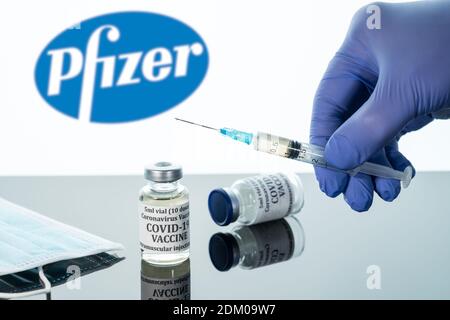 Morgantown, WV - 16 December 2020: Small bottle of coronavirus vaccine with syringe with background of Pfizer logo Stock Photo