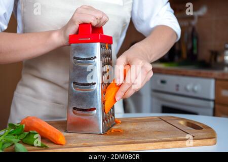 https://l450v.alamy.com/450v/2dm0b0r/female-hands-are-rubbing-fresh-orange-carrots-on-a-steel-silver-grater-grated-carrots-woman-chef-prepares-ingredients-for-cooking-chef-in-an-apron-2dm0b0r.jpg