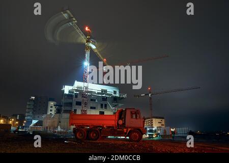 Red illuminated truck against contruction site with cranes. Building activity on contruction site at evening. Stock Photo