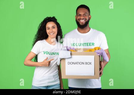 Two Volunteers Holding Donation Box Standing Over Green Background Stock Photo