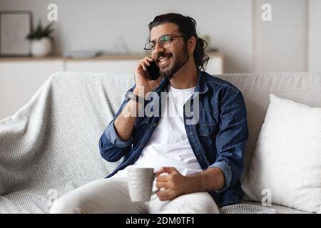 Domestic Leisure. Arab Guy Talking With Friends And Drinking Coffee At Home Stock Photo