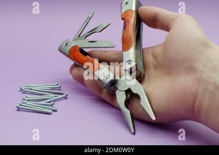 multitool turned into pliers, knife, screwdriver in the hand on violet background, screw. repairing. fix Stock Photo