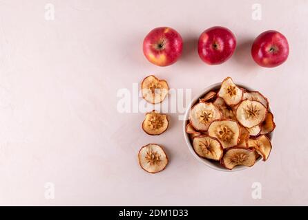 A bowl of dried apple pieces and a few ripe red apples on a light surface. The concept of useful products. Selective focus, copy space, wiew from abov Stock Photo