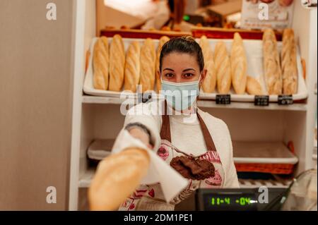 Young bakery owner wearing surgical mask bread background. New normal concept. Stock Photo