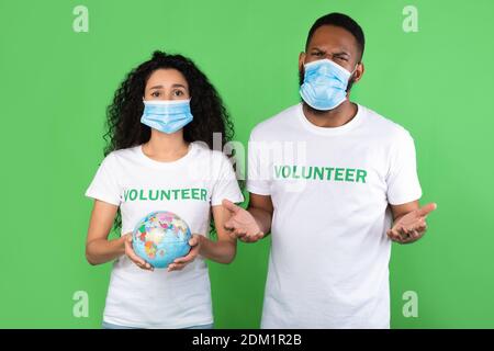 Two Volunteers Holding Globe Wearing Face Masks Over Green Background Stock Photo