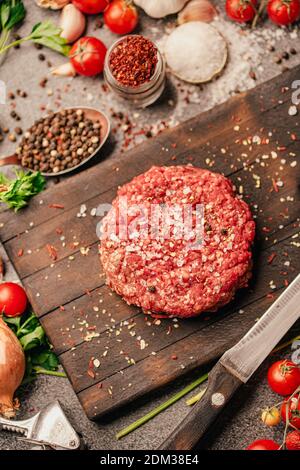 Round ground beef portioned beef patty made from beef mince on a wooden board. Hamburger meat seasoned and ready for a barbecue.Spices and condiments Stock Photo