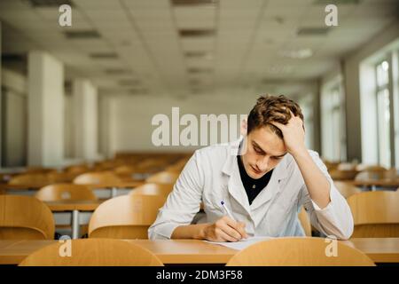 Medical professional filling out a document, looking exhausted, tired. Doctor writing an opinion.Medicine exam, medical practitioner taking test evalu Stock Photo