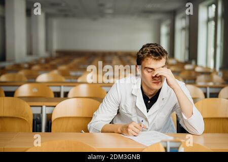 Medical professional filling out a document, looking exhausted, tired. Anxious doctor writing an opinion.Medicine exam, medical practitioner taking te Stock Photo