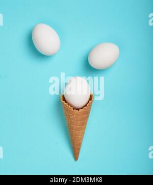 White chicken eggs in a waffle horn on a blue background, top view, flat lay, minimalist trend Stock Photo