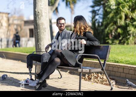 A closeup shot of a woman and a disabled young man with foot prosthesis sitting outdoor Stock Photo