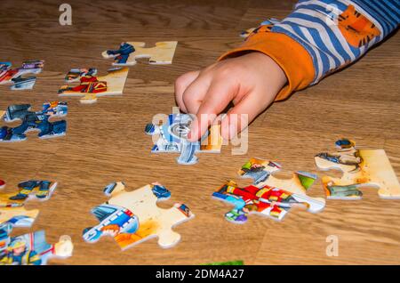 Children's hand with puzzle pieces on wooden surface Stock Photo