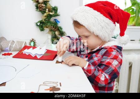 child girl in Santa hat making christmas card from paper Stock Photo
