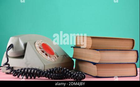 Retro rotary telephone, stack of books on a desk isolated against a blue pastel wall Stock Photo