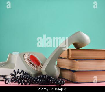 Retro rotary telephone, stack of books on a desk isolated against a blue pastel wall Stock Photo