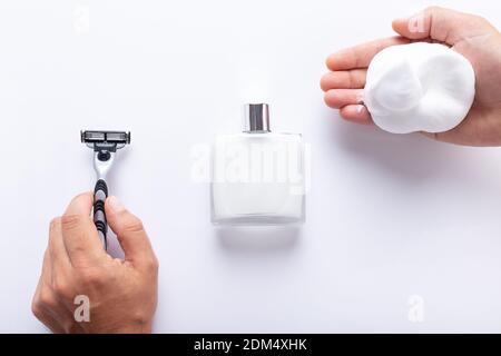 Hands holding razor blade and shaving foam, with after shave isolated on white background top view. Shaving products for men. Stock Photo