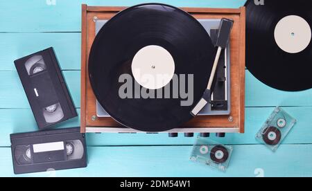 Vintage vinyl player with plates, video cassette, audio cassette on a blue wooden background. Top view. Retro media technologies Stock Photo