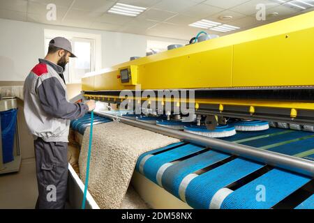 Man operating carpet automatic washing machine in professional laundry service Stock Photo