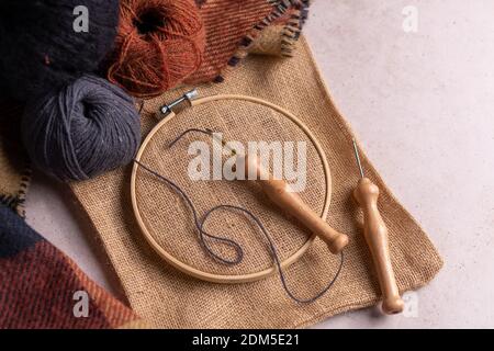 Flat lay composition of punch needle tools on a concrete surface in warm tones. Different sizes of needles, embroidery hoops, scissor and colorful thr Stock Photo