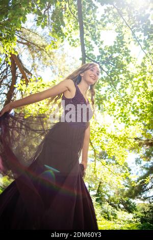 A naturally beautiful young women with long blonde hair dressed in a purple ball gown runs and twirls having fun in a countryside setting. Stock Photo