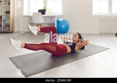 Cheerful sporty young female lying on gym mat at home and doing bicycle crunches Stock Photo