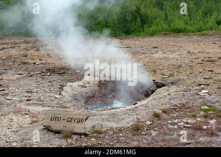 Steam and smoke rises from Litli Geysir in the Haukadalur valley, part of the Golden Circle in Iceland. A sign with the name can be seen on the ground. Stock Photo