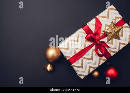 Christmas and New year gift box wrapped in festive paper and decorated with red ribbon with bow on black background. Stock Photo