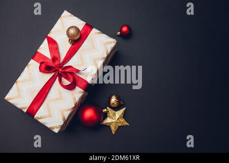 Christmas and New year gift box wrapped in festive paper and decorated with red ribbon with bow on black background. Stock Photo