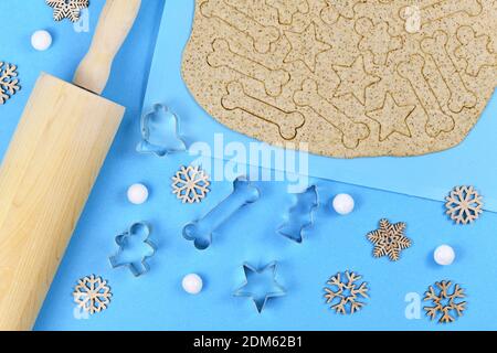 Baking Christmas cookies for dogs. Bone, star and gingerbread man shaped cookie cutters surrounded by raw rolled out dough Stock Photo