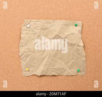 brown piece of torn paper pinned with iron buttons on a brown cork board, copy space Stock Photo