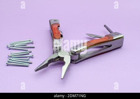 wooden multitool turned into pliers, knife, screwdriver on violet background, screws. repairing. fix Stock Photo