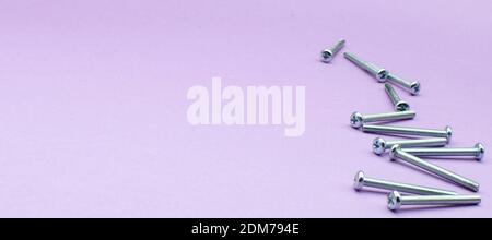 Silver screws laying on violet background, repairing. fixing. nails Wide place fot text Stock Photo