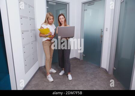 Full length shot of two female entrepreneurs talking in the corridor of workplace, using laptop Stock Photo