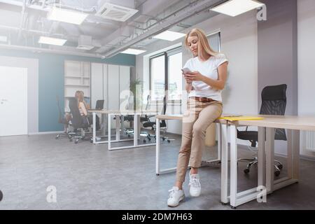 Full length shot of a female entrepreneur using her smart phone, colleagues on background Stock Photo