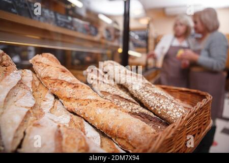 Delicious freshly baked bread in a basket, female bakers working on background Stock Photo