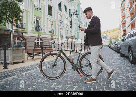 Full length shot of a stylish hipster mature man crossing the street with his bike, using smart phone Stock Photo
