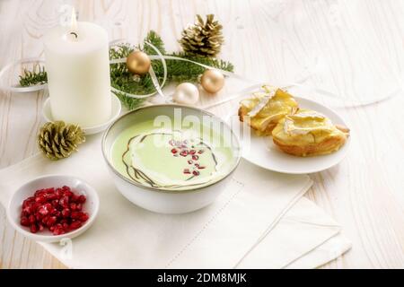 Cream soup from apples and peas with pomegranate seeds and baked camembert canapes, appetizer for a holiday meal on a white wooden table with burning Stock Photo