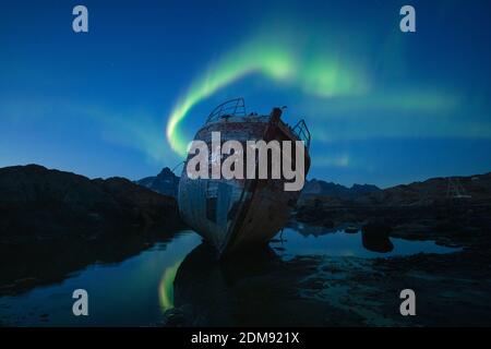 Northern Lights - Aurora Borealis in sky over boat wreckage, Tasiilaq, Greenland Stock Photo