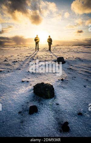 Two people walking at sunrise on black sand beach in Iceland in winter Stock Photo