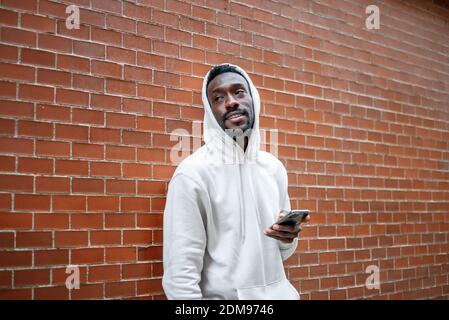 Side shot of African man with happy gesture and hood using smartphone in city Stock Photo