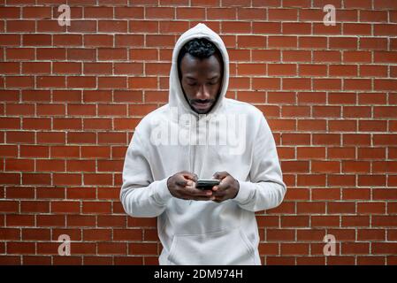 Front shot of African man with serious gesture and hood using smartphone in city Stock Photo