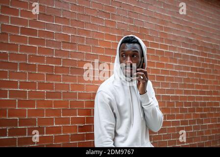 Side shot of African man with serious gesture and hood using smartphone in city Stock Photo