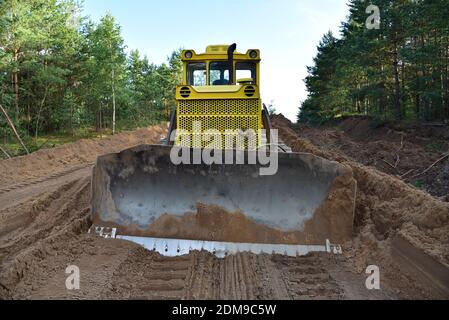 Dozer during clearing forest for construction new road . Yellow Bulldozer at forestry work Earth-moving equipment at road work, land clearing, grading Stock Photo