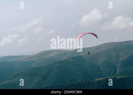 Paraglide silhouette flying over Carpathian peaks and clouds. Stock Photo