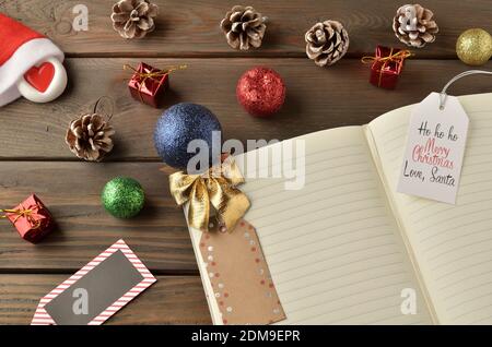 Notepad with space for text and new year greetings with decorations of colorful balls, cones on a brown wooden old brown wooden table. Stock Photo